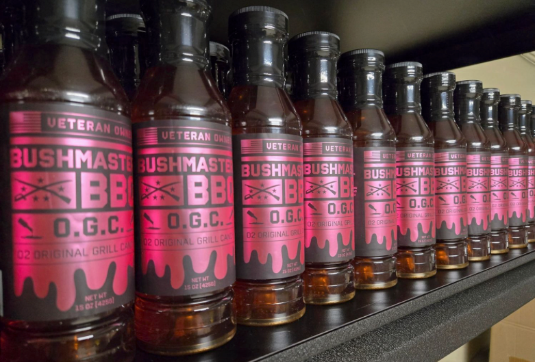 Row of Bushmaster BBQ sauce bottles with red labels on a shelf.